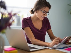 Young woman with glasses looking at tablet and sitting with laptop